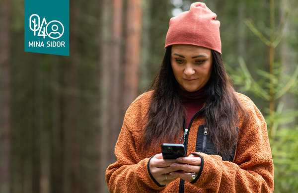 Kvinna i mössa och fleecejacka tittar på sin mobiltelefon i skogen. Foto: Bulldozer